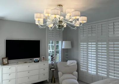 A white bedroom with a bed, dresser, and tv.